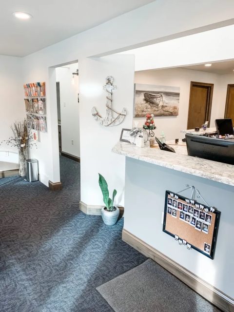 Dental office reception area at Algoma Family Dentistry featuring a welcoming desk, decorative anchor, patient information display, and a cozy atmosphere.